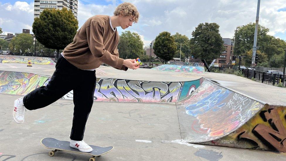 George Scholey rotating puzzle cubes on a skateboard