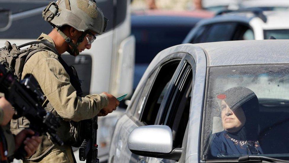 Israeli soldier checks Palestinian driver's ID at a checkpoint near Hebron