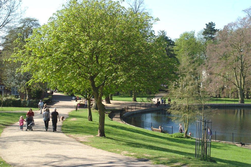 People walking along paths next to the duck pond in Christchurch Park in Ipswich