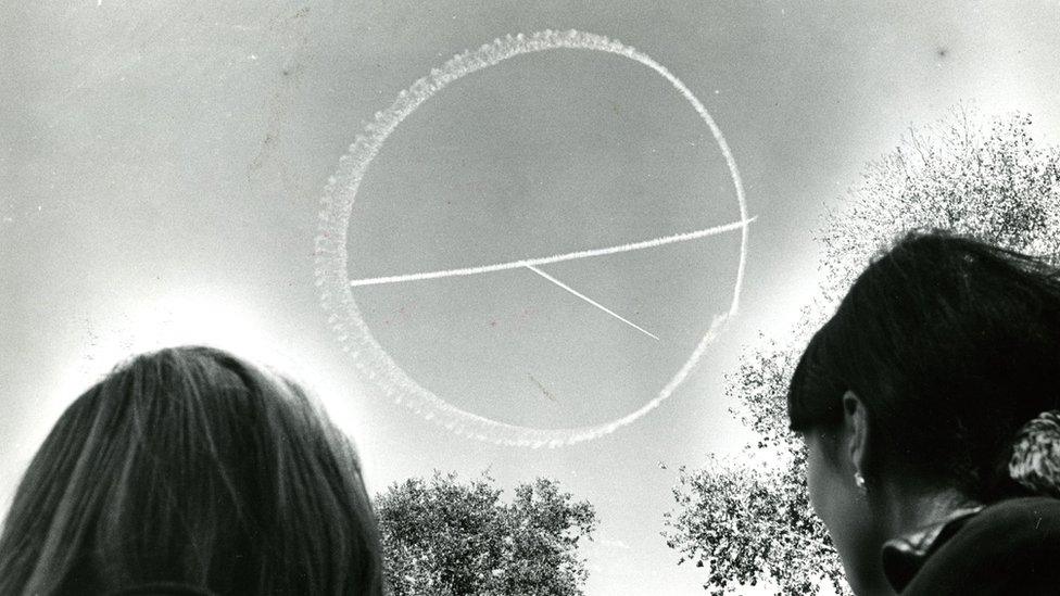 A small skywriting plane draws the peace symbol in the clear blue sky over Boston Common