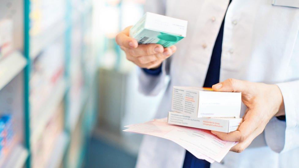 pharmacist takes box of pills from shelf