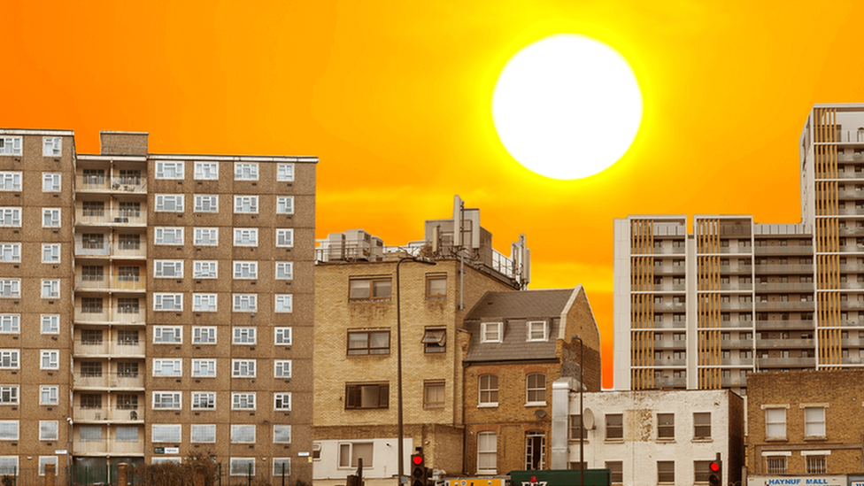 A street with lots of high rise buildings with a strong orange sun in the background