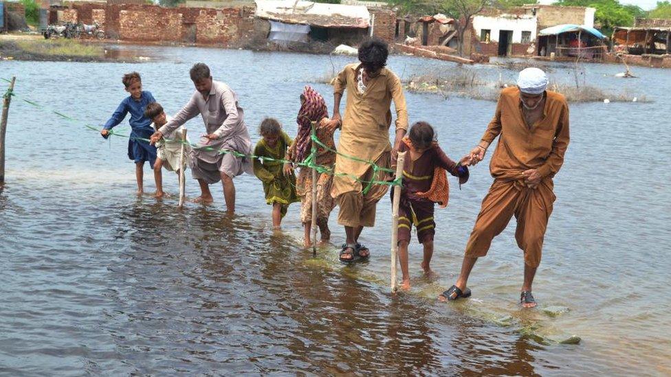 People wade through a flooded area following heavy rains in Sanghar District, Sindh province, Pakistan, 28 August 2022