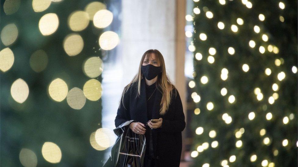 A woman wearing a face mask, with festive lighting on trees in the foreground