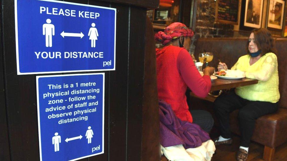 A sign outlining social distancing is displayed near customers in Jackson's Bar in the city centre of Glasgow on October 8, 2020