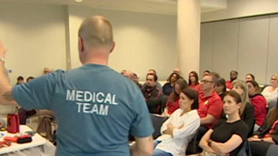 A man wearing a "medical team" t-shirt gives training to a group of students