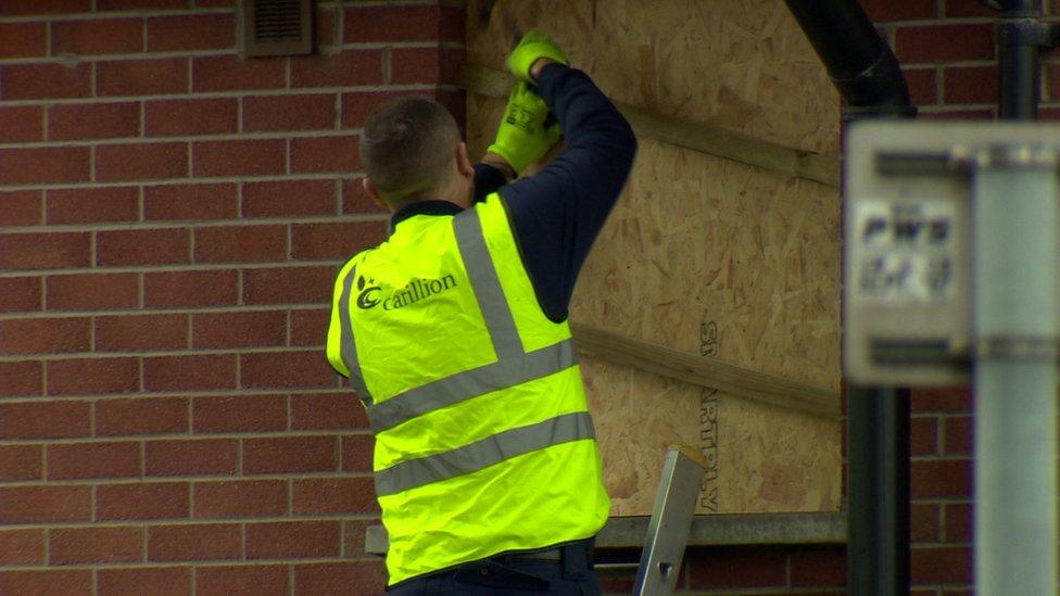 A worker boards up a house close to a bonfire