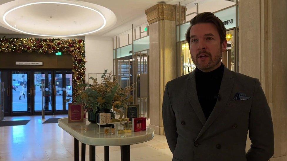 Image of Steven Medway in a black top and tweed jacket standing in a foyer in Harrods