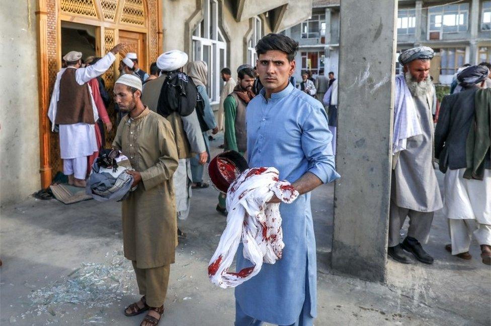 Afghan men hold the belongings of worshippers at the scene of an attack that targeted a mosque in the outskirt of Kabul, Afghanistan, 14 May 2021.