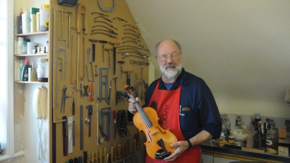 Colin Garrett holding a violin in a workshop