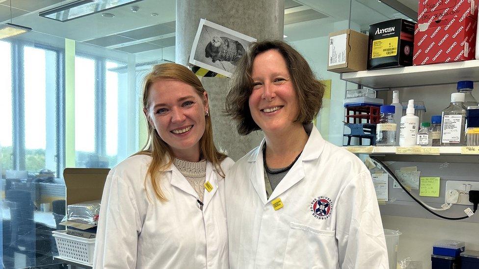 Mrs Brett and Prof Ottersbach at the medical facility in Edinburgh. Both women are wearing white science coats and are smiling at the camera