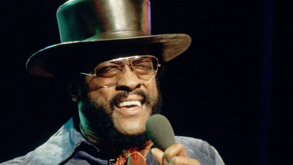 Billy Paul in glasses and a top hat, singing in to a microphone