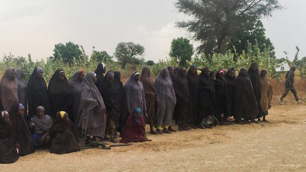 A man carrying a Boko Haram flag walks past a group of 82 Chibok girls, who were held captive for three years by Islamist militants, as the girls wait to be released in exchange for several militant commanders