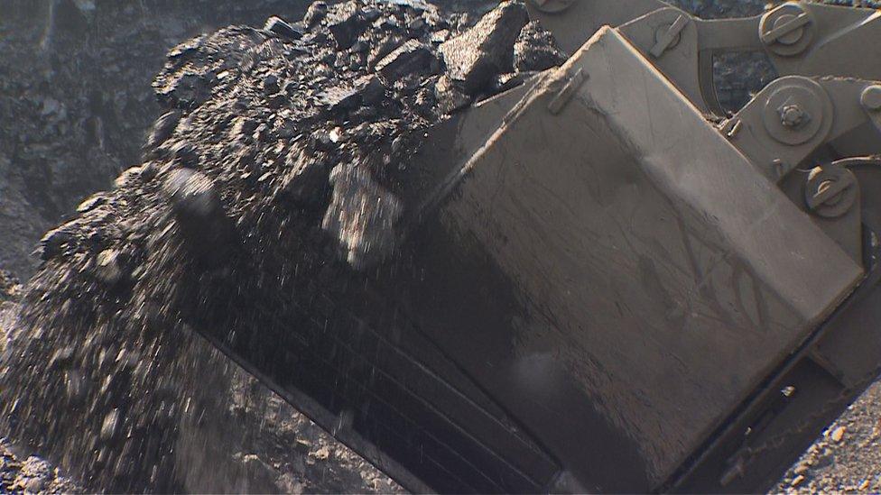 A truck takes giant bites out of a mountain of coal in India