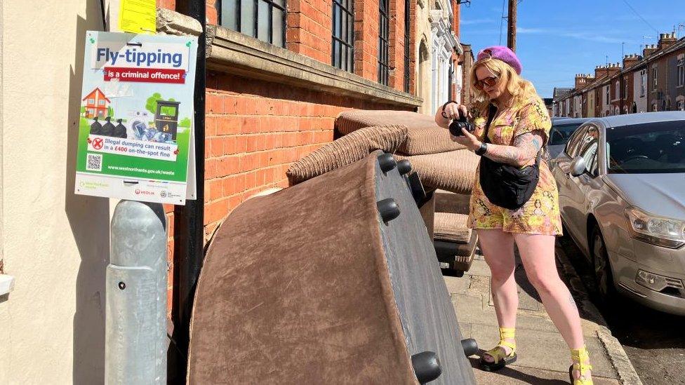 Woman wearing yellow with small purple hat take picture of brown sofa on its side