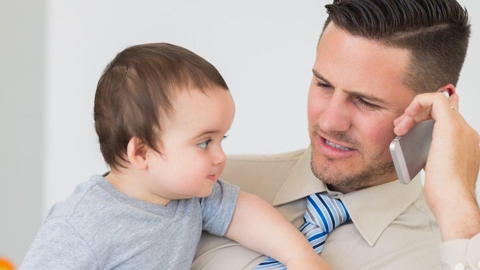 Man on his phone while holding baby