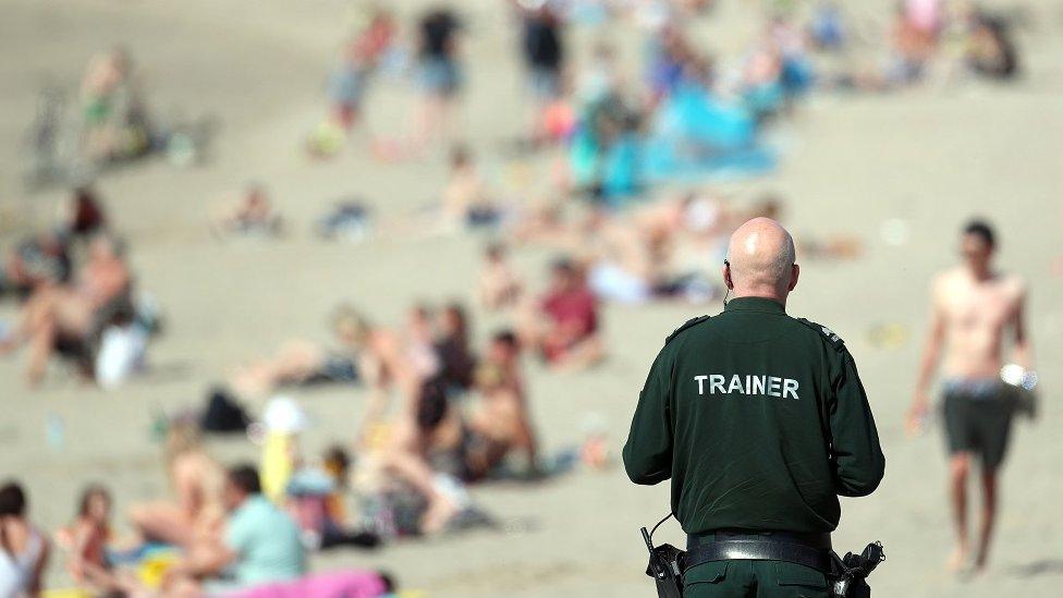 A PSNI officer views the crowd enjoying the Sunday sunshine at Ballyholme beach, Bangor, Co Down