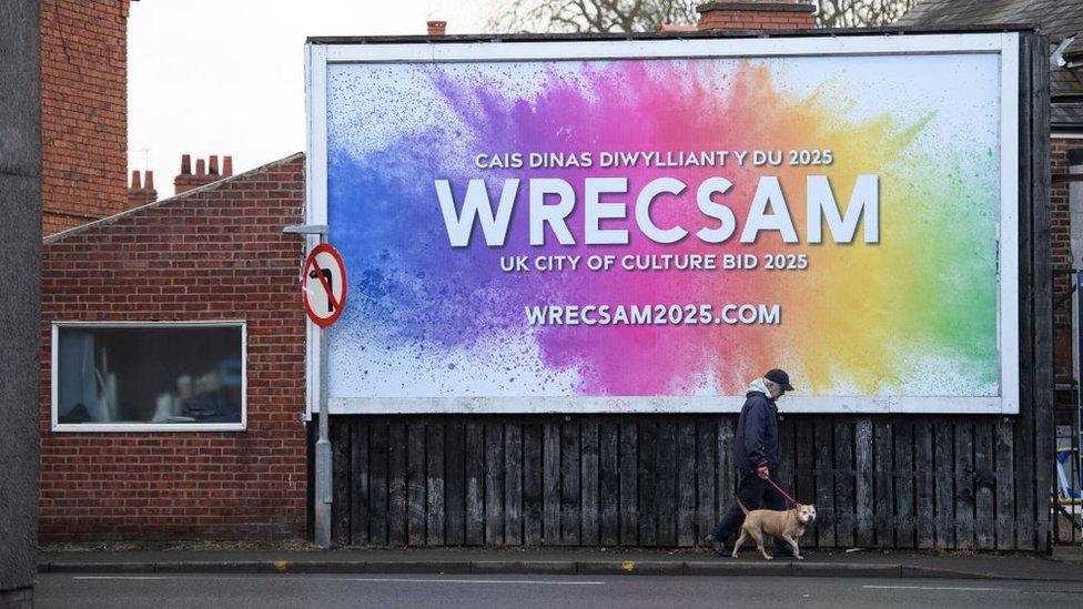 man walking past Wrexham sign