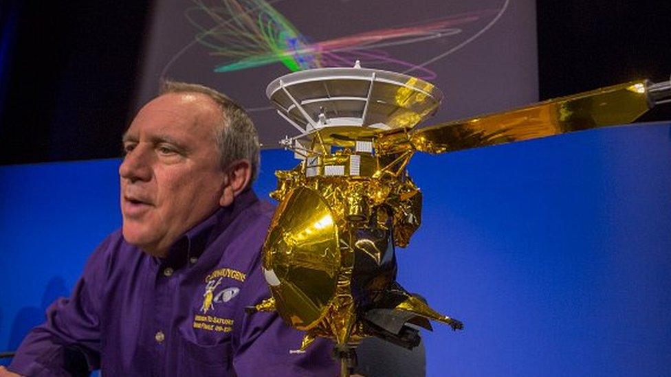 A man sits next to a model of the spacecraft sent to Saturn