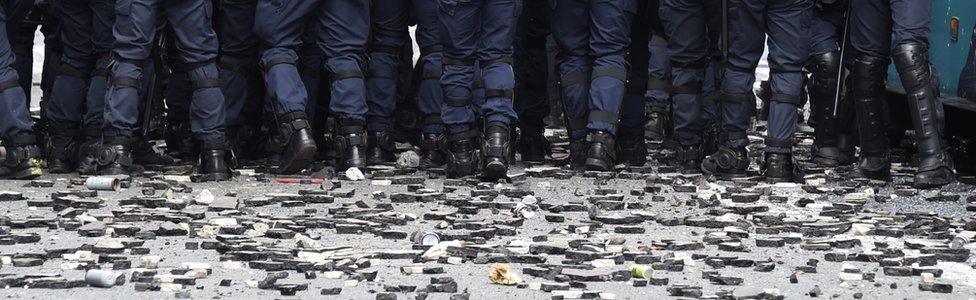 French anti-riot police officers stand as stones and rubbish lie on the pavement during a demonstration against proposed labour reforms near the Hospital Necker in Paris on 14 June 2016