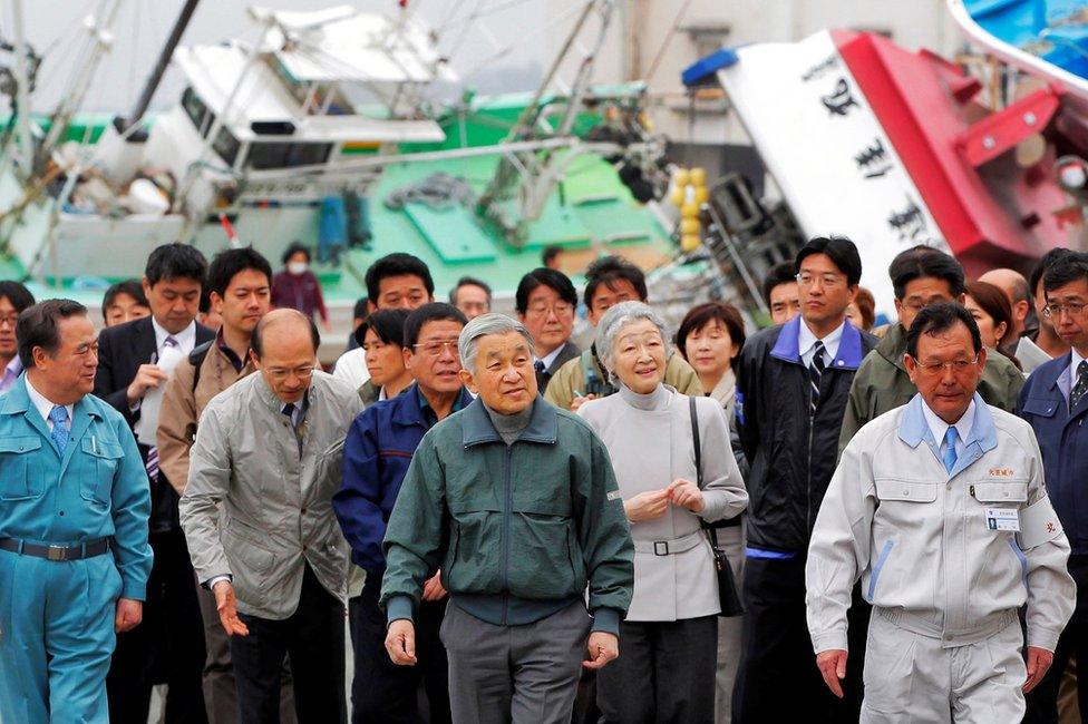 Emperor Akihito (centre) and Empress Michiko (behind Akihito, right), being followed by a number of people, look at overturned ships and the damaged fishing port in Otsu town in Kitaibaraki, about 70km (42 miles) south of the Fukushima Daiichi Nuclear Power Station, 22 April 2011.