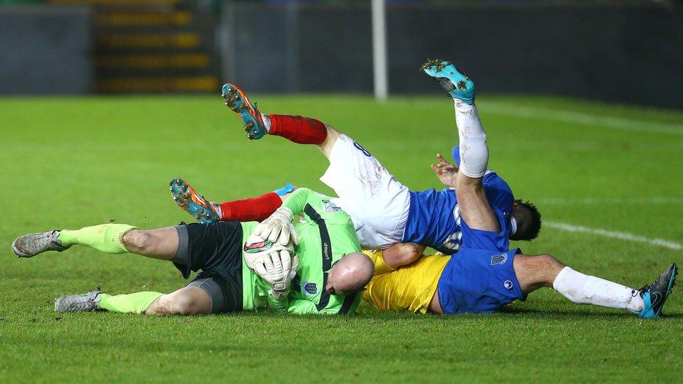 Linfield striker Paul Smyth lands on top of Ballymena United keeper Alan Blayney and defender Johnny Taylor