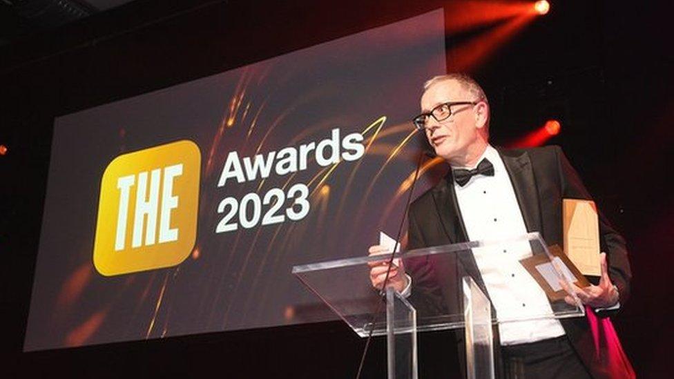 Anglia Ruskin's vice chancellor Roderick Watkins making a speech on stage having scooped the award under his arm