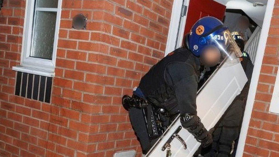 Police officer taking a front door off in a raid on a house