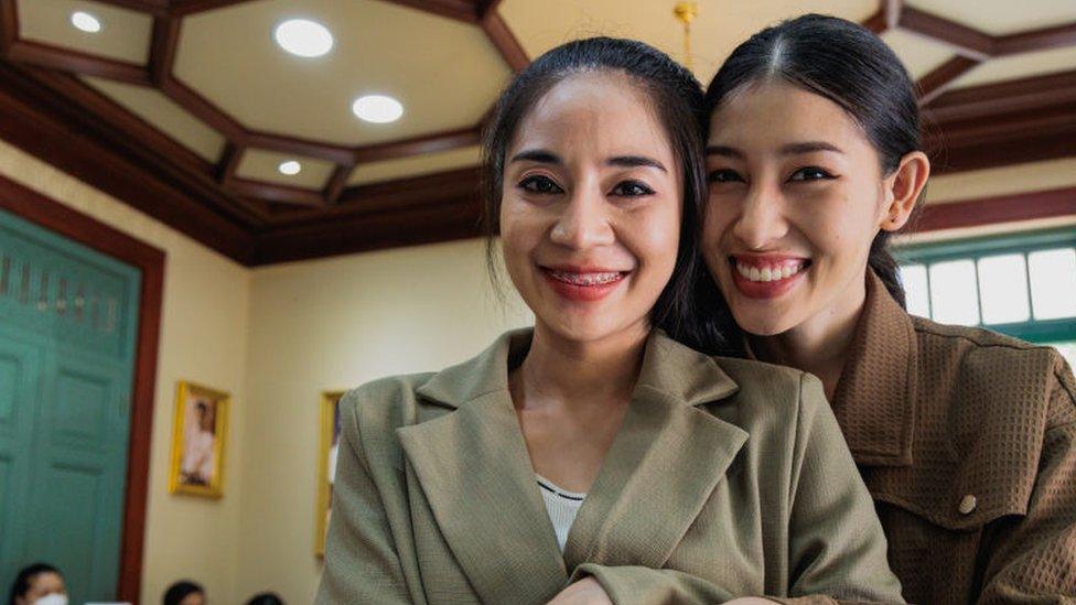 LGBTQ+ couple pose for pictures while holding a civil partnership bill at Sai Suddha Nobhadol Building