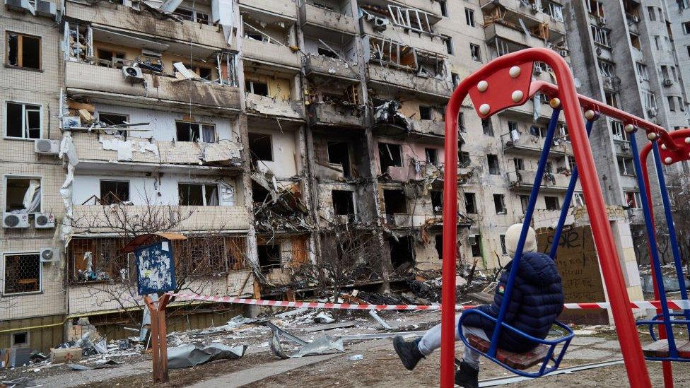 Kyiv bombed building child on swing.