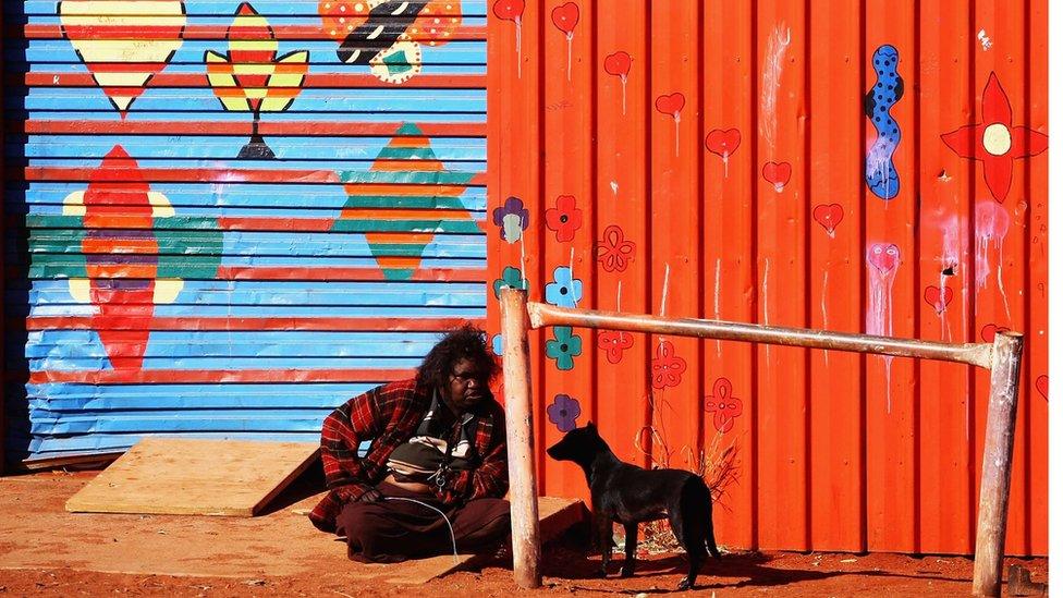 An Aboriginal woman sits on the ground in a remote town in regional Australia