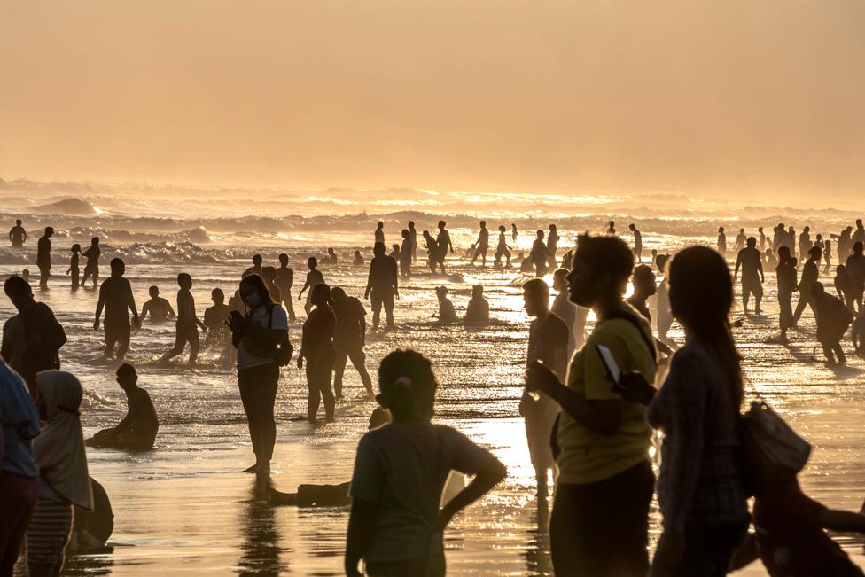 People stand in the ocean surf as the sun sets