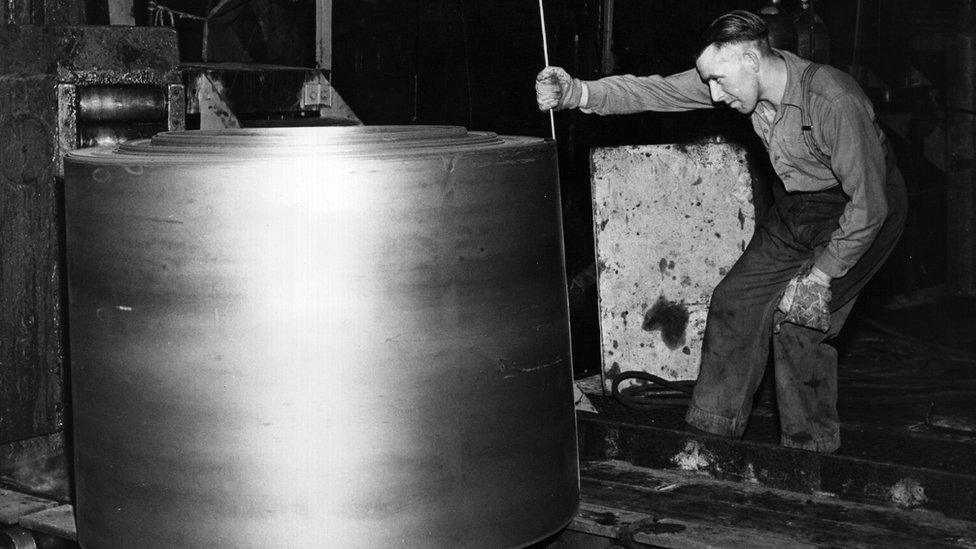 A worker measuring a roll of steel in 1961