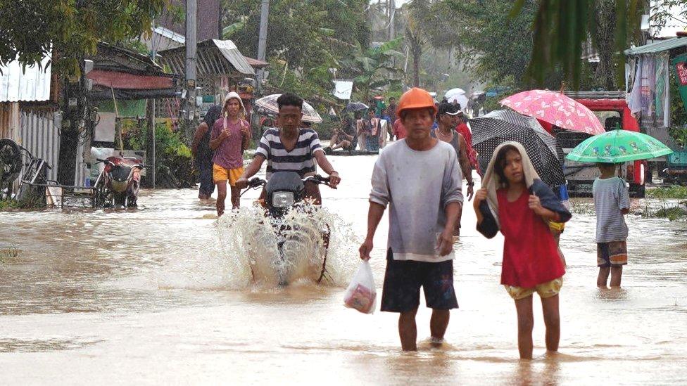 People carrying umbrellas walk through a flooded street