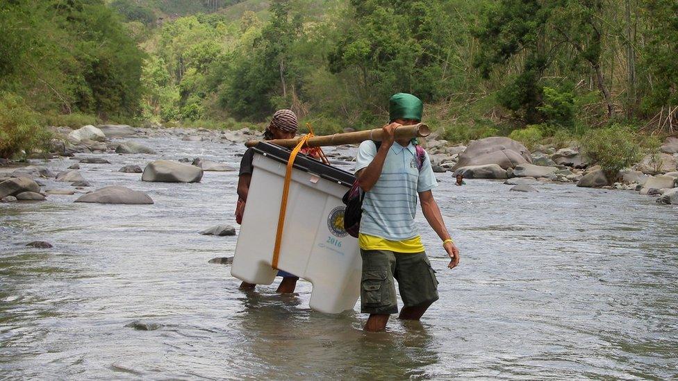 Two Filipino villagers carry a box containing an electronic voting machine, across a river, on Sunday, in the far flung community of North Upi, Maguindanao Province