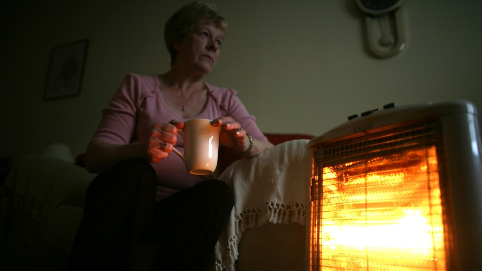 Woman sits by electric bar heater