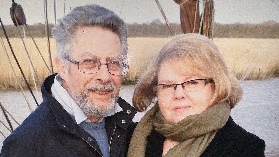 A family photo of Geoffrey Hoad and his wife Anne McDowell, in coats and scarves in front of a body of water