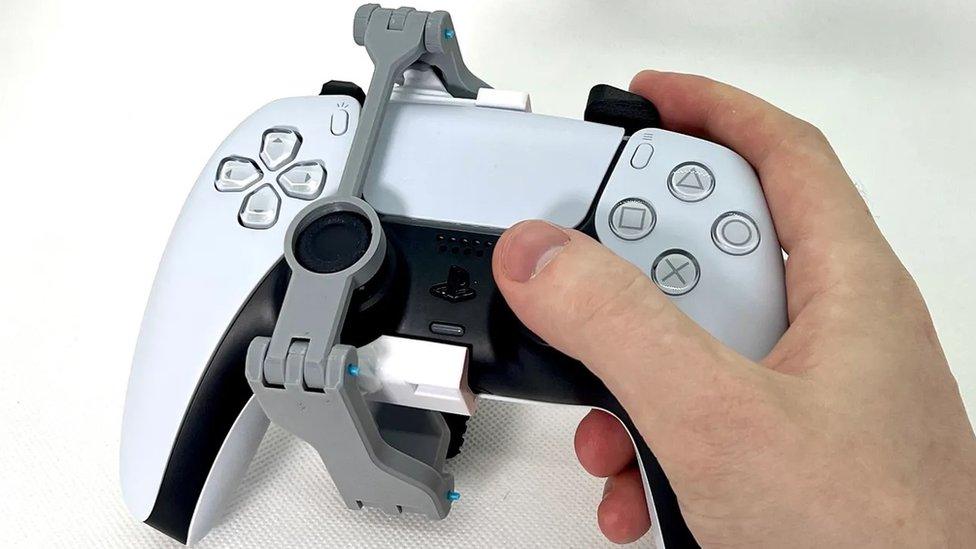 hand holds a white playstation 5 controller with a plastic modfication added to the left joy stick