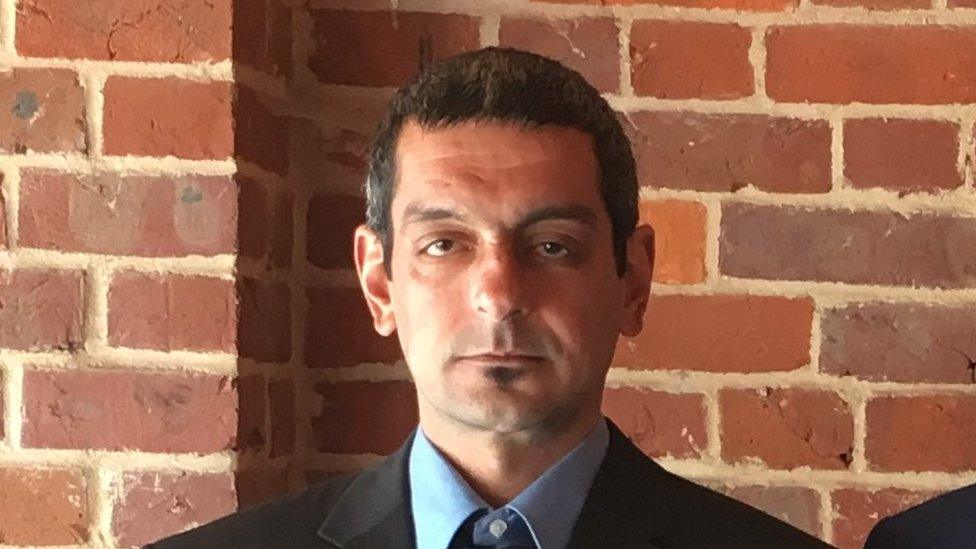 a man in a suit standing in front of a brick wall