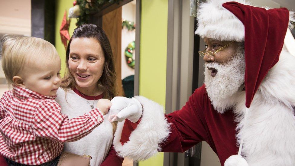 In this Thursday, Dec. 1, 2016 photo, Larry Jefferson, playing the role of Santa, says goodbye to one-year-old Ezra Good with a fist bump as his mother Jennifer of Ramsey watches at the Santa Experience at Mall of America in Bloomington, Minn.