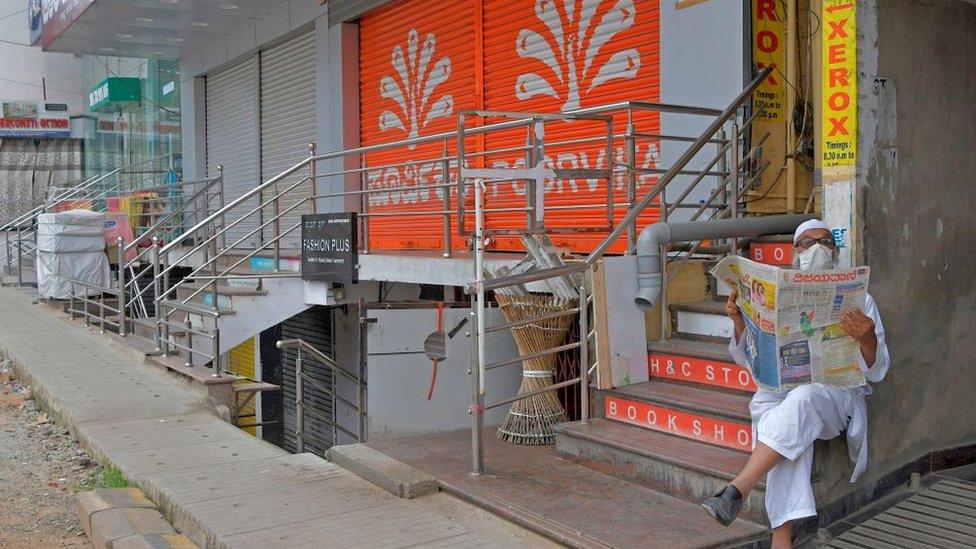 A man reads a newspaper while sitting in front of closed shops in a commercial area during a week-long lockdown to contain the surge of COVID-19 coronavirus cases, in Bangalore on July 15, 2020.