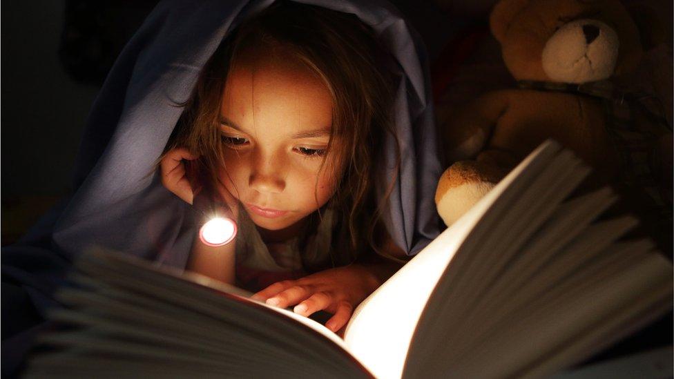 Girl reading under covers