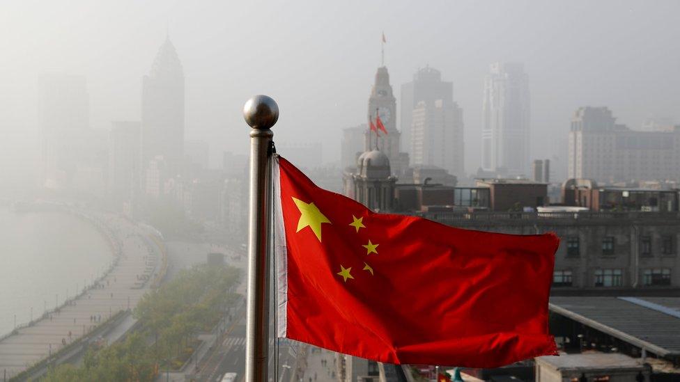 Chinese flag flutters in front of a view of buildings on the Shanghai Bund