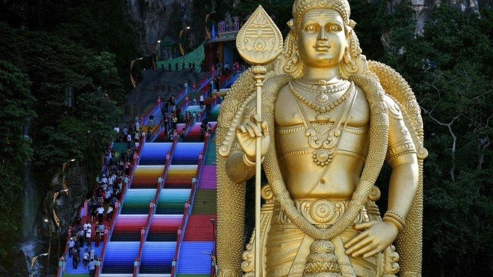 A golden statue stands in front of the colourful stairs at Malaysia's Batu Caves complex