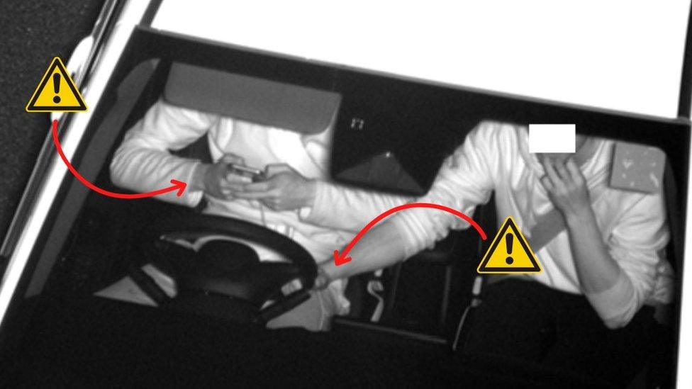 Motorist using a mobile phone while passenger holds steering wheel