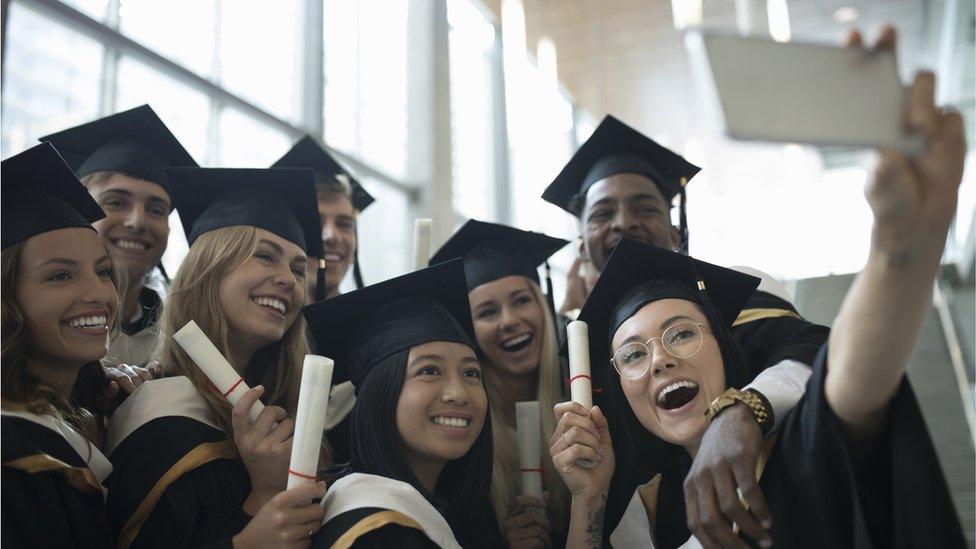 Students in mortarboards pose for a selfie