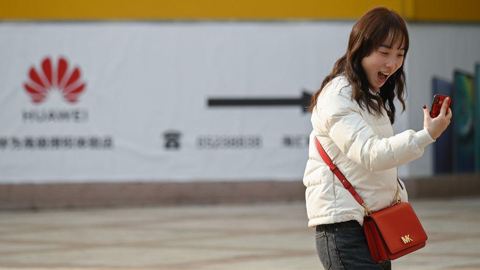 A woman laughs while using her smartphone outside a Huawei store in Beijing on January 29, 2019.