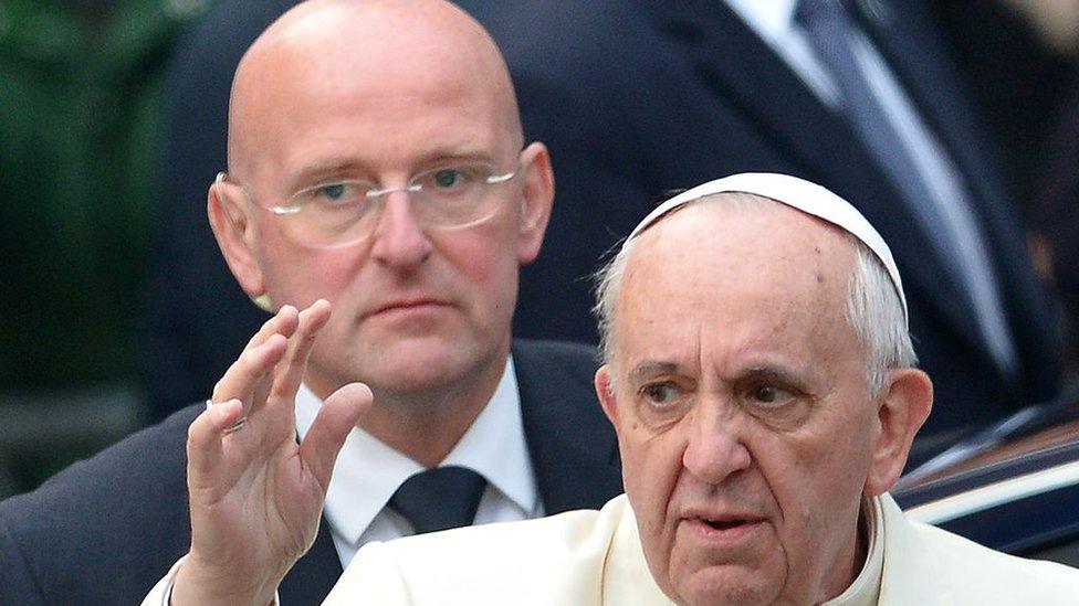 Pope Francis waving, with Domenico Giani behind him