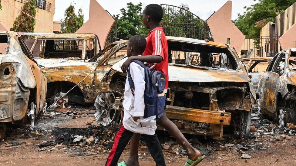 Children walk past burned cars outside the headquarters of president Bazoum's Nigerien Party for Democracy and Socialism in Niamey on August 7, 2023