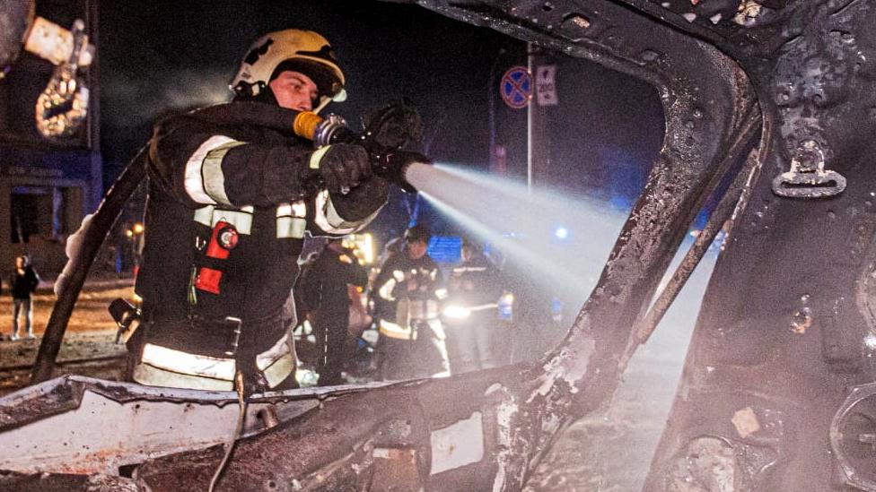 A firefighter douses a burnt car in the aftermath of a Russian missile strike on a hotel in Kharkiv, Ukraine, in this handout image released 11 January 2024